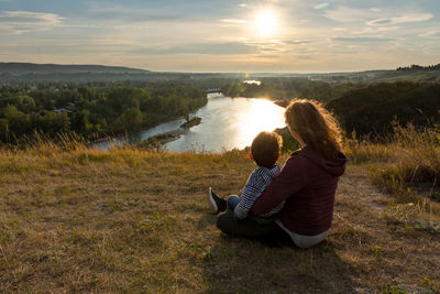 Rear view of couple sitting on shore against sky during sunset