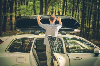 Rear view of man opening luggage carrier of car