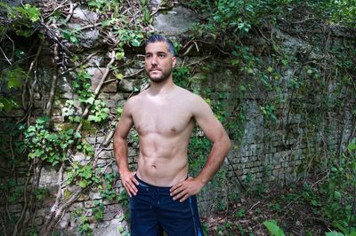 Shirtless man standing by weathered wall