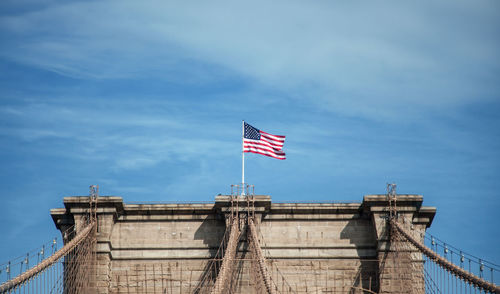 Low angle view of american flag on brooklyn bridge against sky