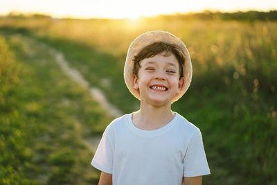 Portrait of a smiling little boy in a white t-shirt and hat playing outdoors on the field at sunset