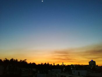 Silhouette trees and cityscape against sky during sunset