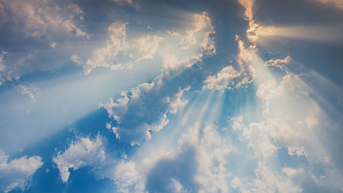 Low angle view of sunlight streaming through clouds