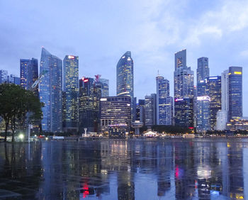 Illuminated city by bay against sky