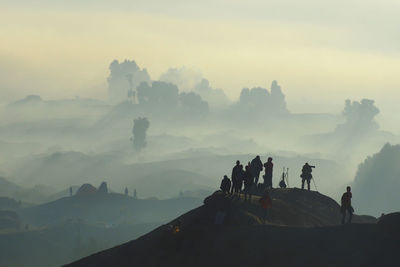 Silhouette people standing on mountain peak during foggy weather