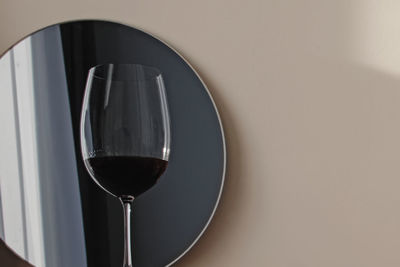 Glass of red wine reflecting in a small round mirror on white wall background