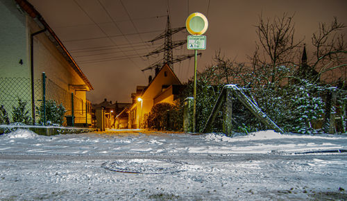 Snow covered trees by illuminated building against sky at night