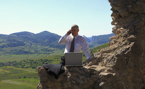 Businessman talking on mobile phone by rock formation against mountains