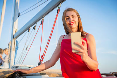 Attractive woman taking selfie photo on smartphone while standing on yacht