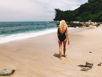 Rear view of woman walking at beach against sky