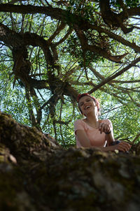 Low angle view of woman sitting on tree trunk