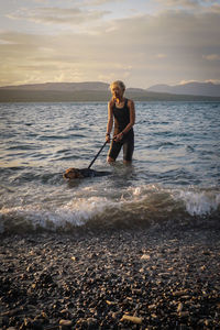 Woman with dog standing in lakewater against sky