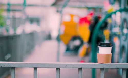 Close-up of metal fence against blurred background  paper coffe cup resting.  