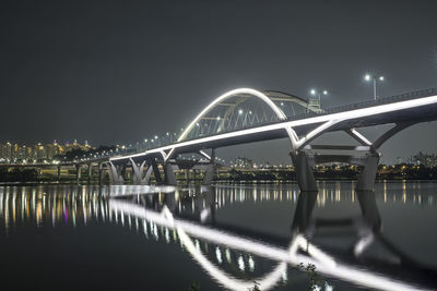 Illuminated bridge over river against sky at night