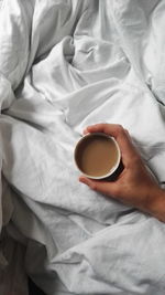 Close-up of hand holding coffee cup on bed