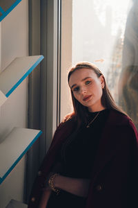 Portrait of young woman standing against window at home