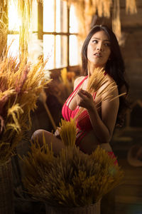 Beautiful young woman standing by flower indoors