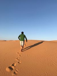 Rear view of man walking on desert against clear sky