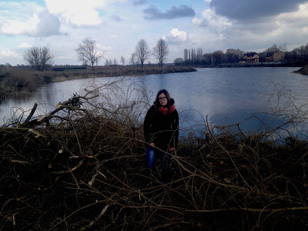 water, lifestyles, leisure activity, person, looking at camera, sky, portrait, young adult, casual clothing, lake, standing, smiling, front view, full length, happiness, sunglasses, river, cloud - sky