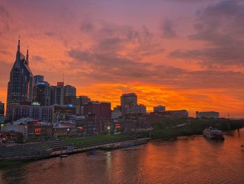 Buildings by river against sky during sunset