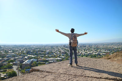 Rear view of man with arms outstretched standing against sky