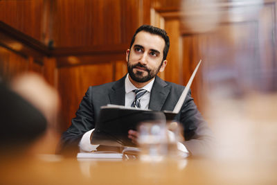 Confident bearded male financial advisor with contract file sitting in board room during meeting