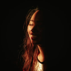 Close-up portrait of a smiling young woman over black background