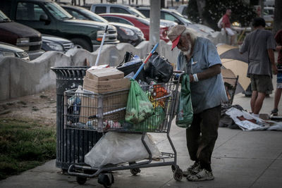 Homeless man with shopping cart standing on footpath