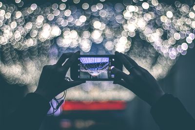 Man photographing illuminated mobile phone at night