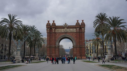 People in front of palm trees against cloudy sky