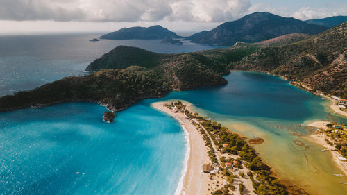 Breathtaking drone view of sandy oludeniz beach located near turquoise sea water and green hills against overcast sky and island on summer day in turkey