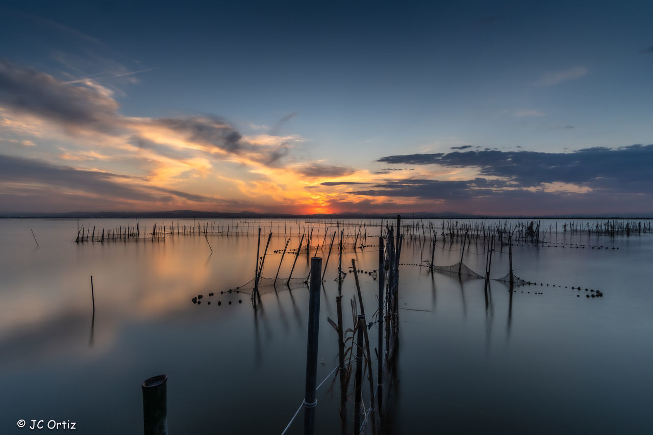 water, sky, reflection, cloud, beauty in nature, scenics - nature, tranquility, sunrise, sea, horizon, nature, tranquil scene, dawn, morning, no people, idyllic, horizon over water, environment, beach, dramatic sky, outdoors, landscape, non-urban scene, blue, travel destinations, land, seascape, pier, sun, wooden post, twilight, silhouette, sunlight