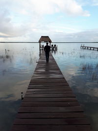 Rear view of people on pier over lake against sky