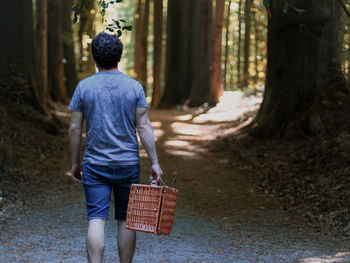 From the back walks along a path among the trees in a public park with a wicker basket