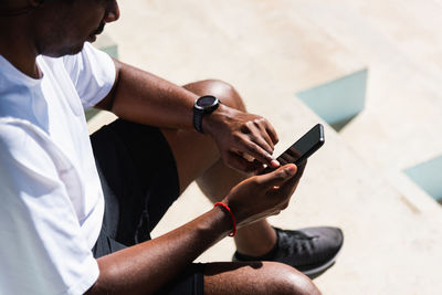 Low section of man using smart phone while sitting outdoors