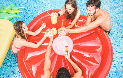 High angle view of friends toasting drinks on red pool raft in swimming pool
