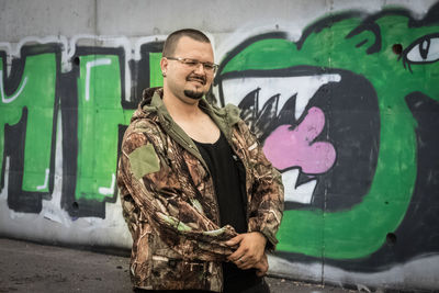 Portrait of young man standing against graffiti wall