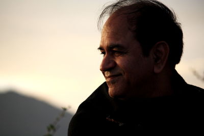 Close-up of smiling man looking away against sky during sunset