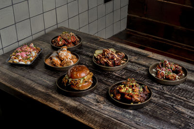 From above of appetizing chicken wings in bbq sauce placed near burger and cheese fries on wooden table in restaurant