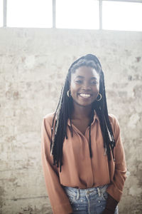 Portrait of young female it expert smiling while standing against wall in office