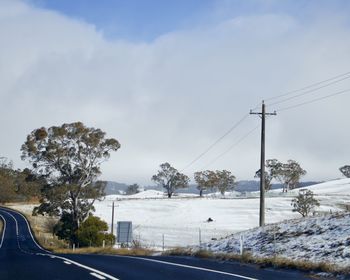 Road by trees against sky during winter