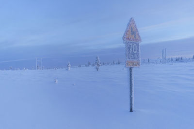 Snow covered road sign against cloudy sky at dusk