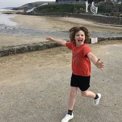 Portrait of cheerful boy with arms outstretched running at beach