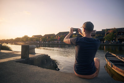 Man photographing hoi an cityscape. tourist with smart phone in ancient city at sunset, vietnam.