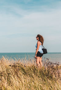 Side view of woman standing on field against sea and sky