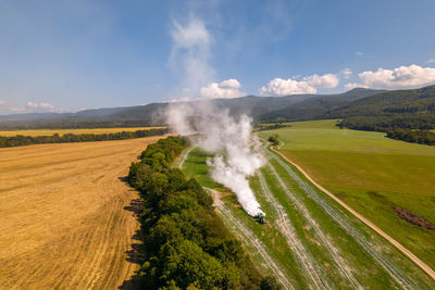 Aerial view of a tractor spreading lime on fields to improve soil quality after the harvest. 