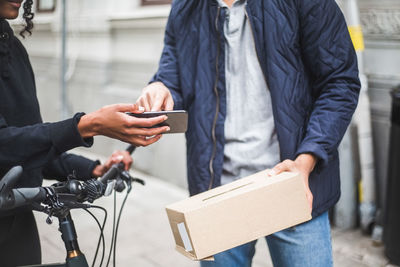 Midsection of delivery woman taking sign from male customer while delivering package on sidewalk in city