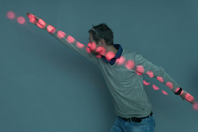 Pink light on man standing with arms outstretched against wall