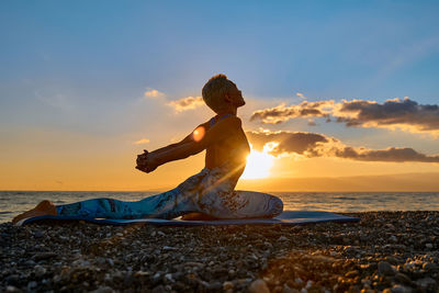Woman practing yoga on the beach in sunrise.