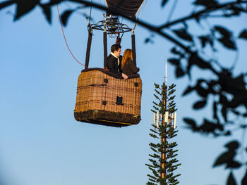 Low angle view of man hanging on tree against sky